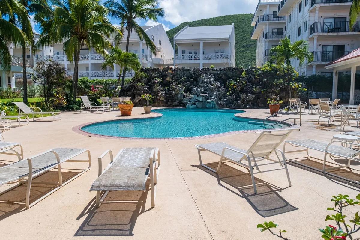 A pool with loungers and a stone water feature below balconied apartments