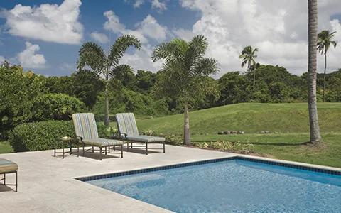 A rectangular pool and two loungers on a terrace at Four Seasons Nevis, open lawn and palms beyond