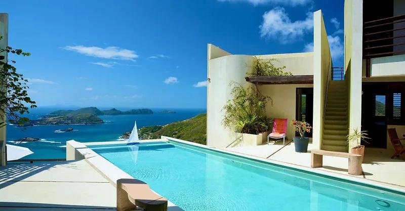 A pool beside a curved-walled villa looking out over islands and open sea
