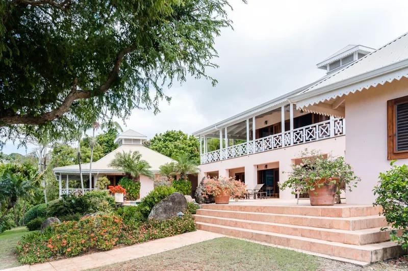 A pink colonial house with a white verandah, steps rising through a flowering garden