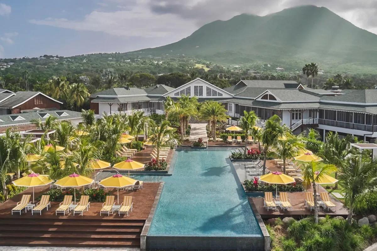 The Four Seasons Nevis pool terrace lined with yellow umbrellas and loungers, Nevis Peak rising behind the resort