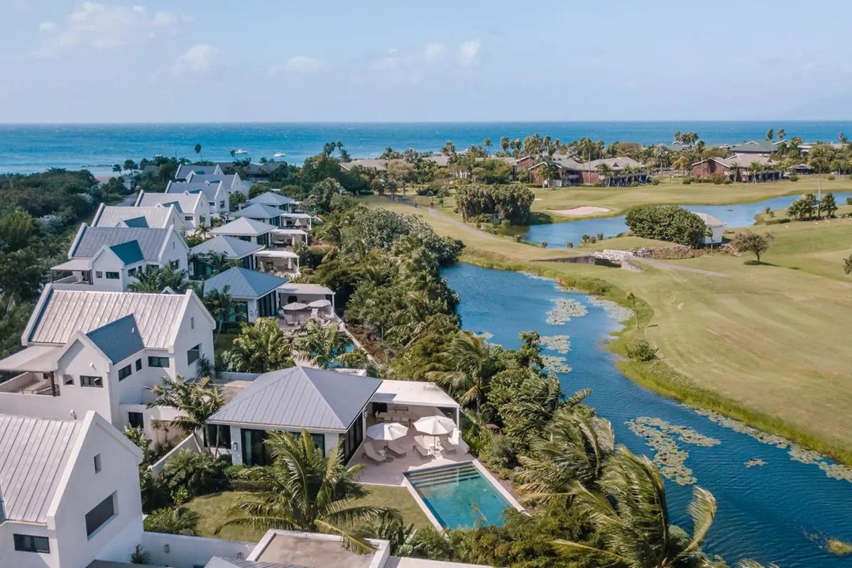 White villas between a golf course and a lagoon, the sea beyond, seen from the air
