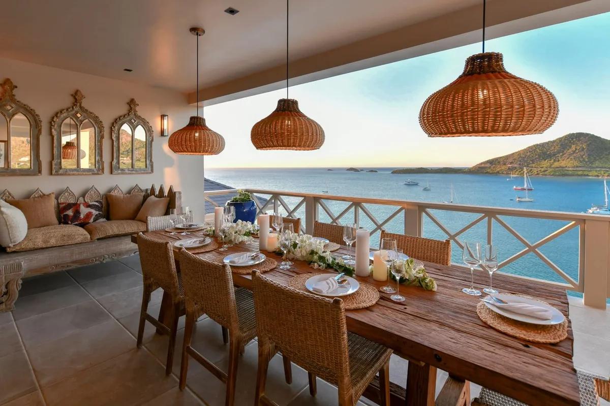 A long dining table under woven rattan pendants in an open-sided room looking out to the sea at Reeds Point, Antigua