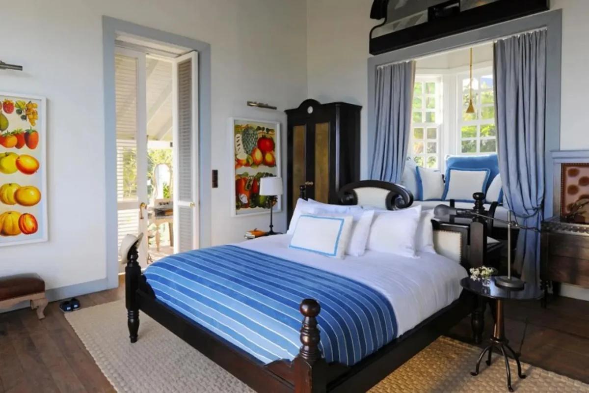 A bedroom with a dark timber bed under a blue striped cover, framed fruit paintings on the wall