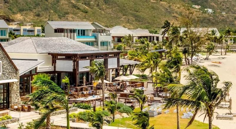 Low resort buildings and timber pavilions among palms along a grey-sand beach