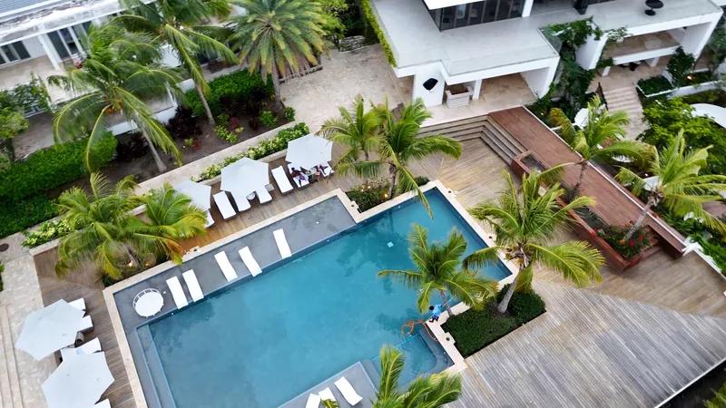 A resort pool with loungers and cabanas among palms, seen from above