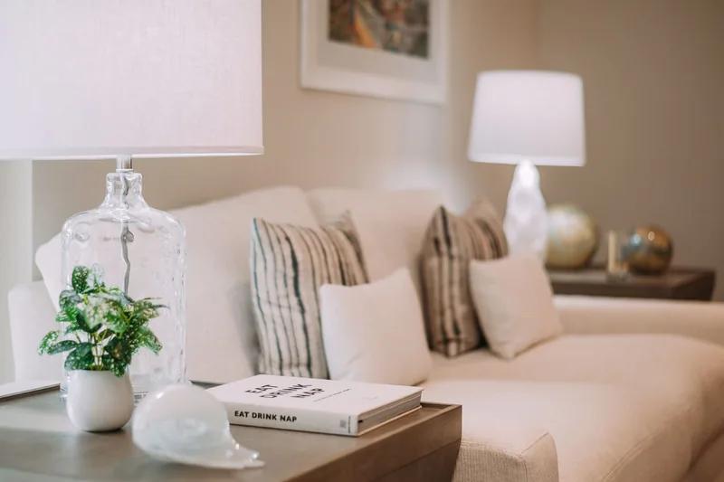 A corner of a pale sofa with two table lamps, a book and a potted plant