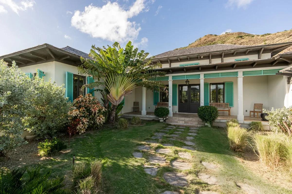 A single-storey villa with turquoise shutters and a stone path across the lawn