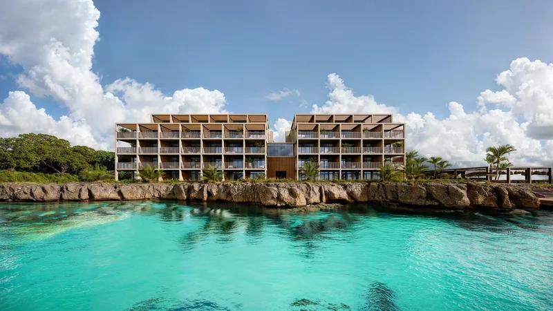a timber-clad building on a rocky shore above a turquoise cove