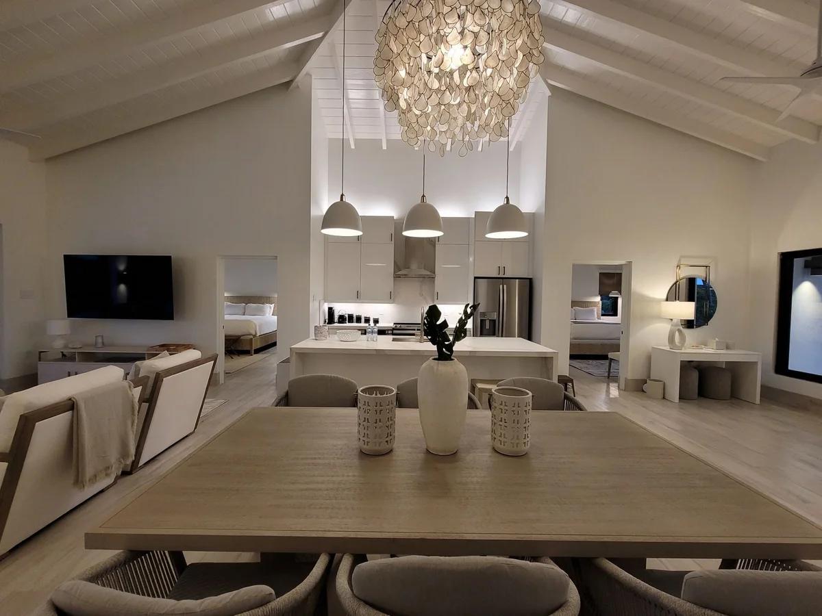 A white open-plan dining and living room under a vaulted ceiling with a shell chandelier
