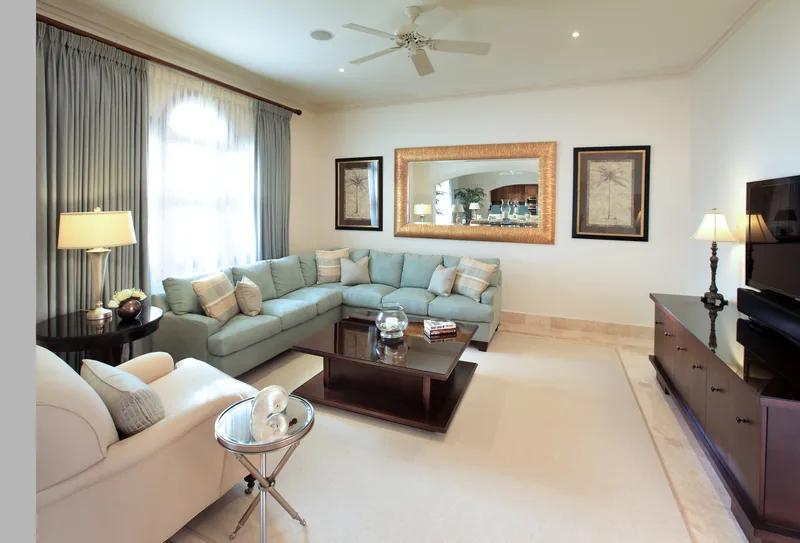 A pale living room with sage upholstered sofas, a gilt mirror and a dark timber cabinet