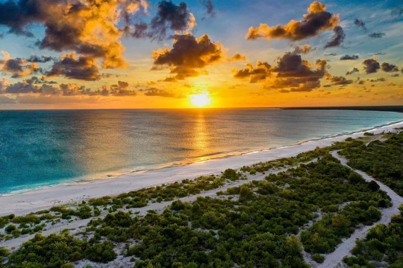 Sunset over a long dune-backed Barbuda beach, the sun low on the horizon