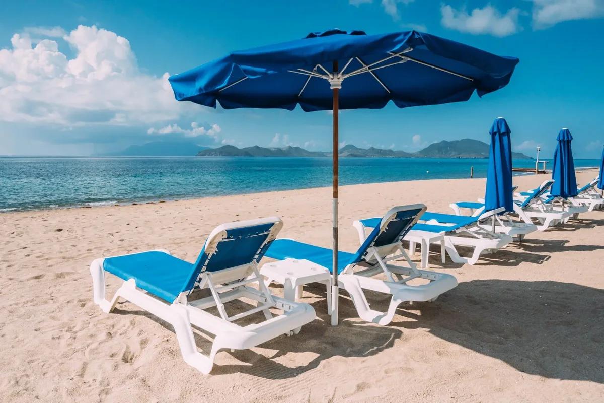 Blue parasols and loungers on a pale beach, an island rising across the channel
