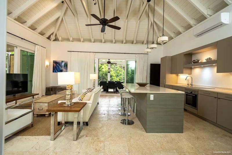 An open kitchen and living room under a white vaulted ceiling with a dark ceiling fan