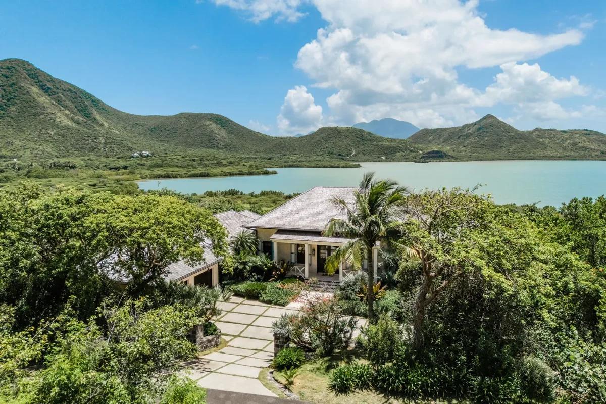 A hip-roofed villa set in dense green above a salt pond, hills rising behind