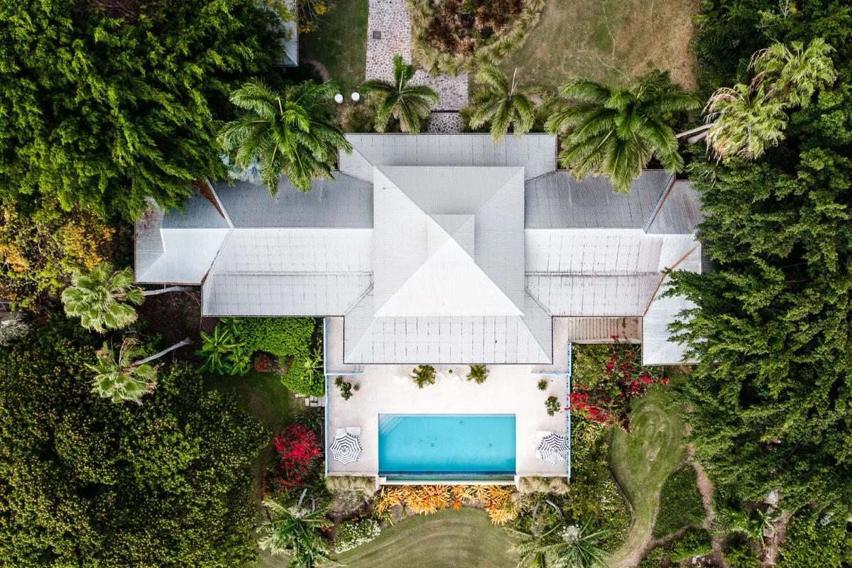 A hipped white roof and turquoise pool seen from directly above, surrounded by dense garden