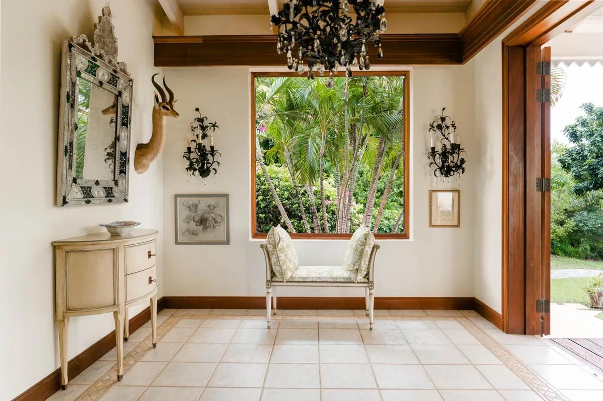 A tiled entrance hall with a gilt mirror, console table and chandelier, a window looking into the garden