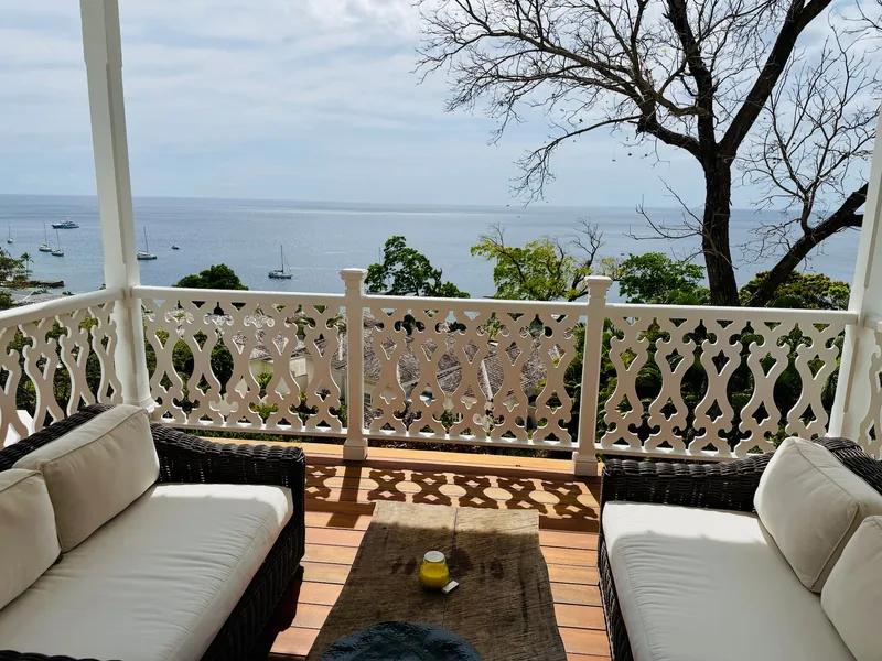 A verandah with wicker seating behind a white fretwork balustrade, the bay beyond