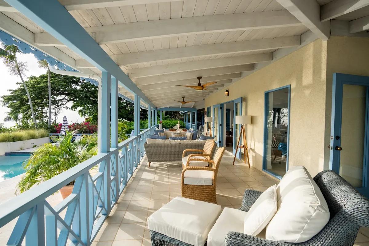 A long verandah with pale blue rails and rattan seating running the length of the house