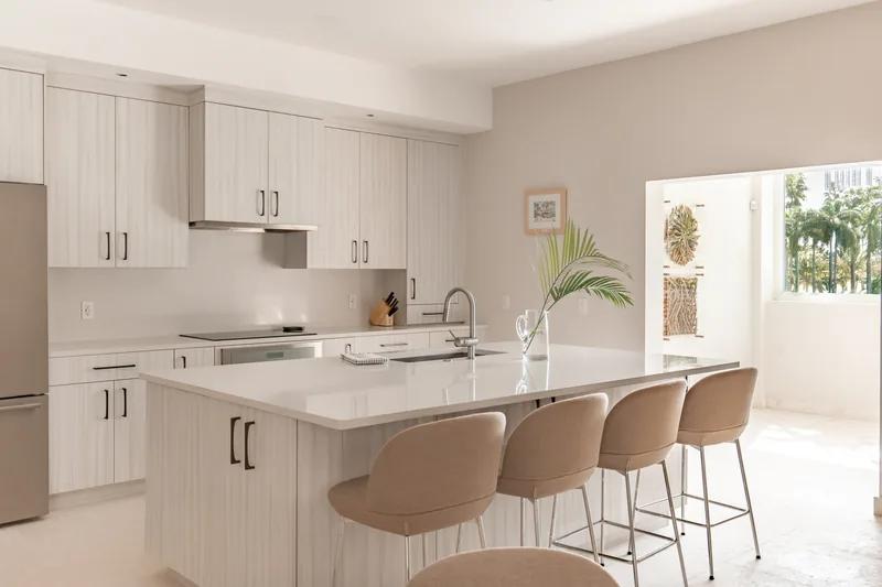 A white kitchen with a stone island and four upholstered stools