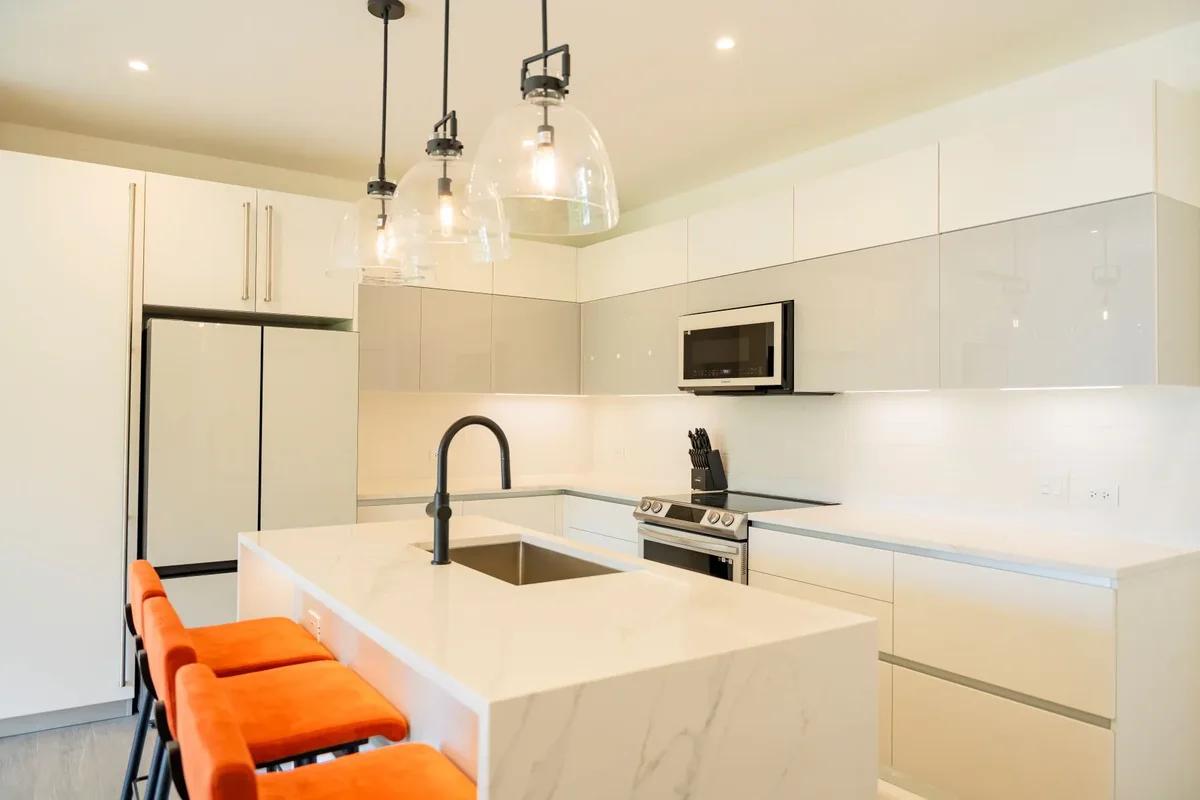 A white kitchen island with bright orange bar stools and a black tap