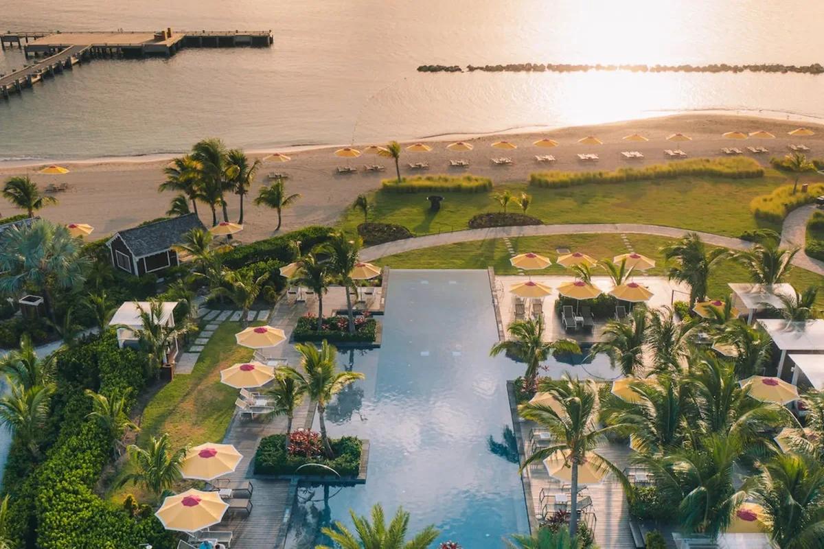 Artist’s rendering of a resort pool with parasols beside a beach at dusk, a jetty running out to sea