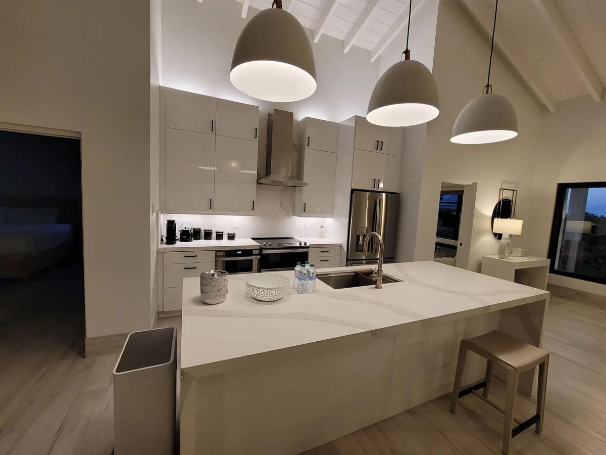 A white kitchen with a long island under three dome pendant lights