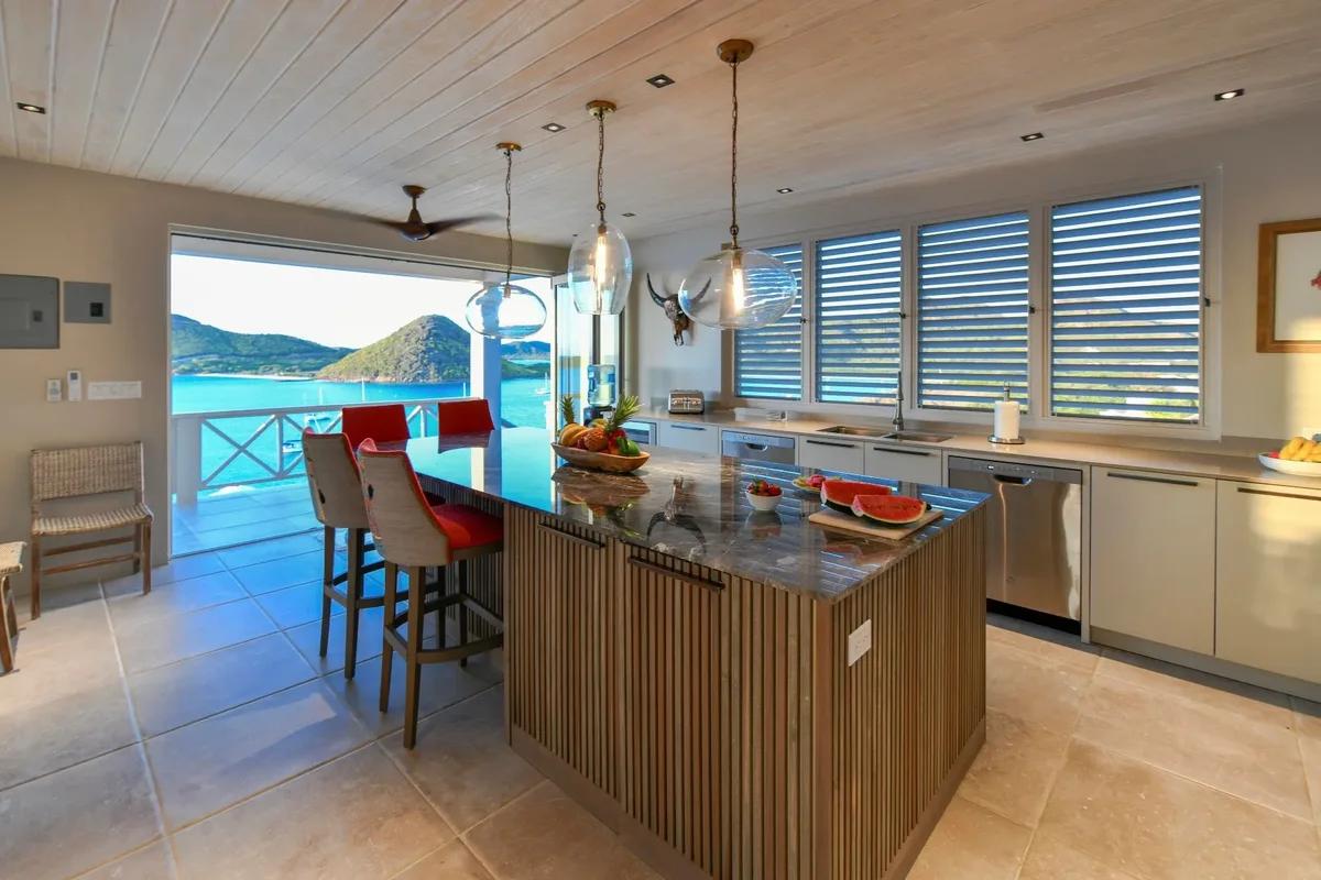 A kitchen island with red bar stools, opening through to a terrace above the sea