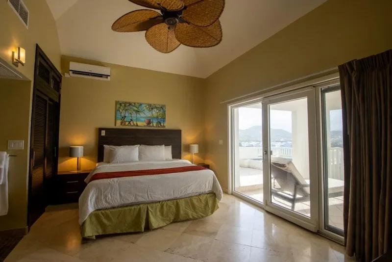 A bedroom under a palm-leaf ceiling fan, sliding doors opening to a balcony