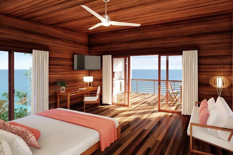 A timber-lined bedroom with a coral throw on the bed, doors folded back to the sea