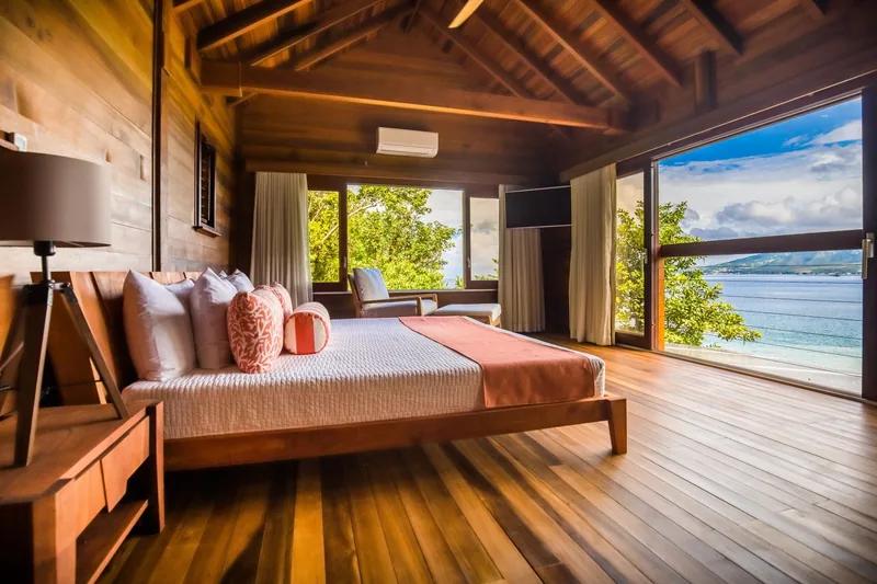 A timber-lined bedroom under a vaulted ceiling, its wall open to the sea