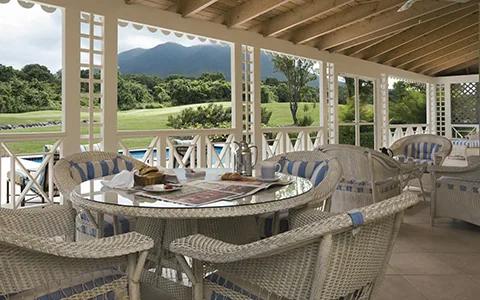 A screened verandah with a glass dining table looking out to the golf course and Nevis Peak