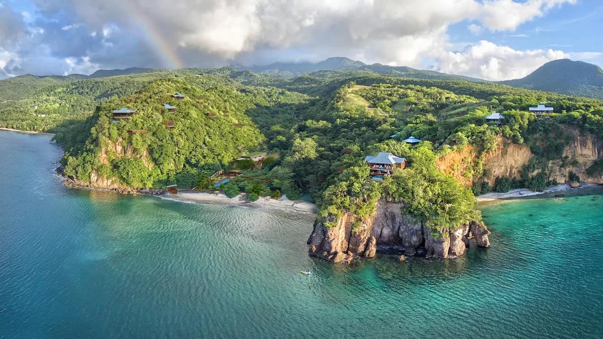 A rocky islet off Dominica's forested coast, a rainbow above the ridge behind