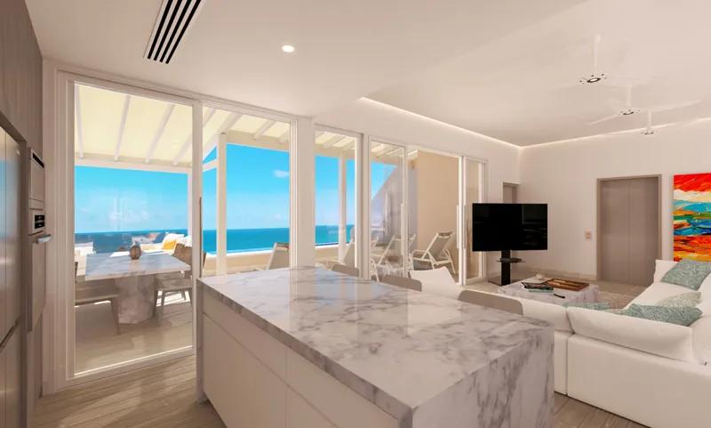 A marble kitchen island in an open-plan room, the sea through the windows beyond