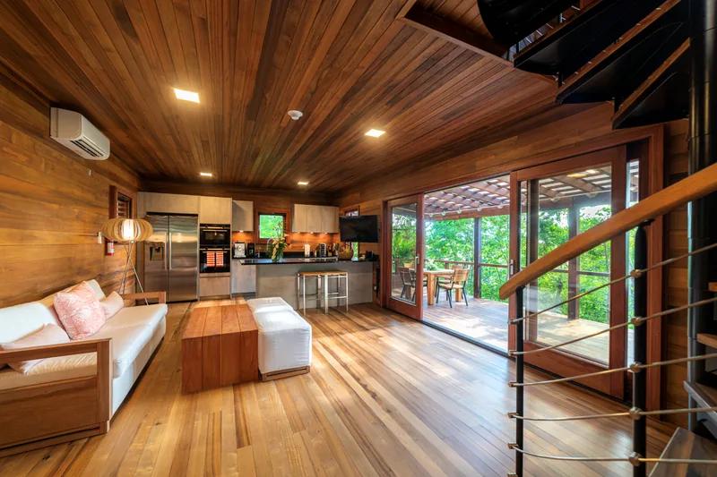 A timber-lined kitchen and living space with a mezzanine rail and doors to the forest