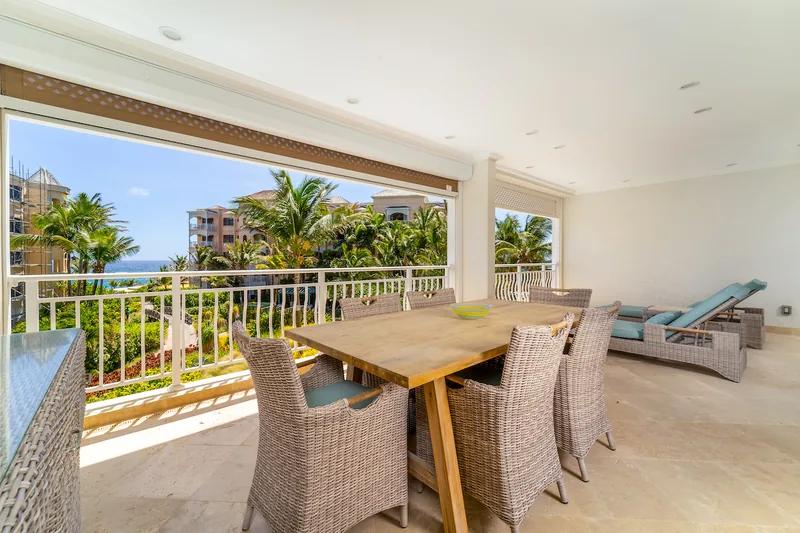 A dining table and wicker chairs on a covered terrace, the sea beyond the balustrade