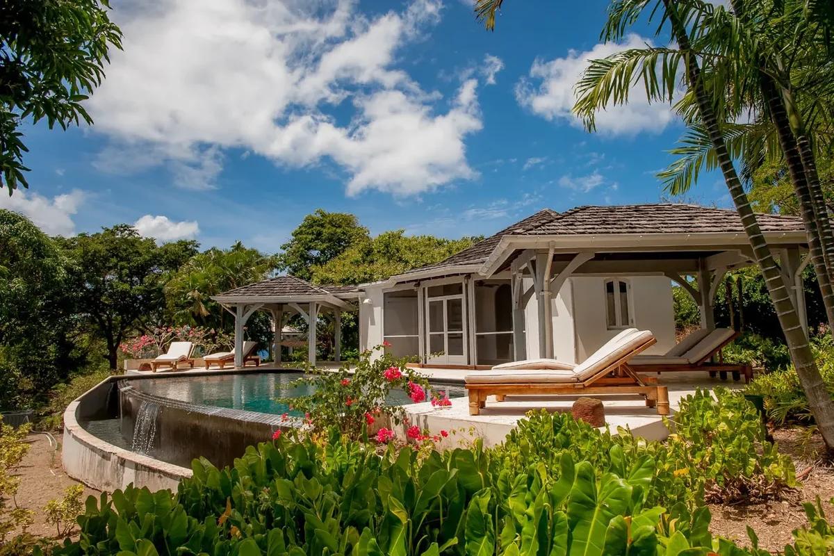 A villa with a timber pergola above a curved pool, heliconia and palms around it