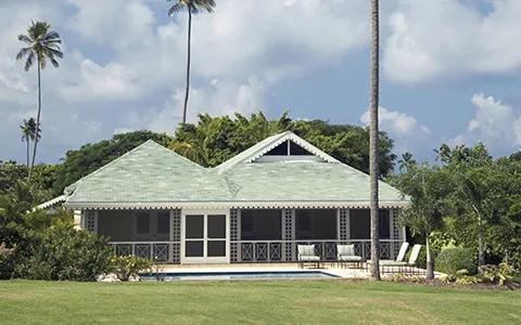 A green-roofed bungalow with a screened verandah on a lawn among tall palms