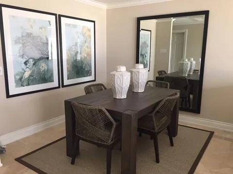 A dining table and rattan chairs below framed prints and a tall mirror