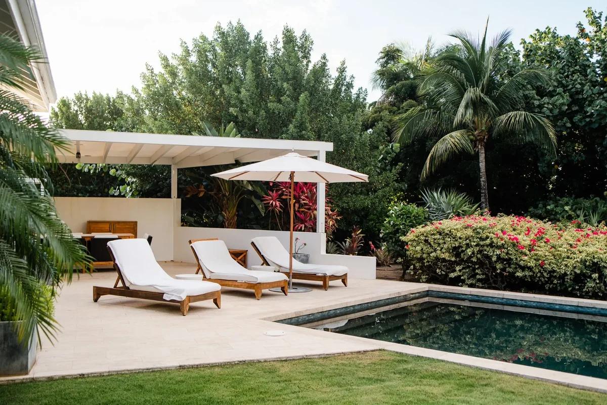 Two loungers and a parasol beside a pool enclosed by flowering hedges