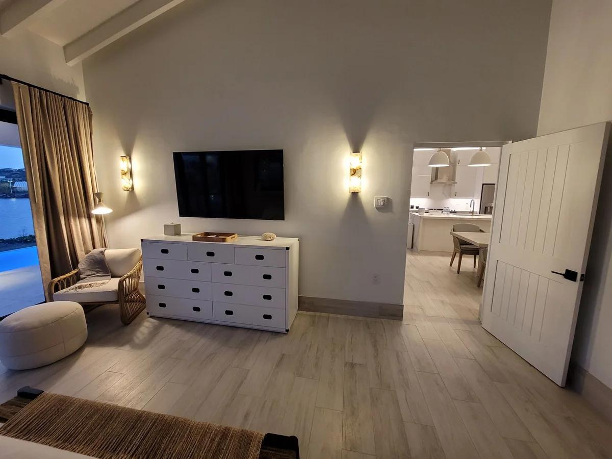 A bedroom with a wall-mounted television above a dresser, an ensuite through the doorway