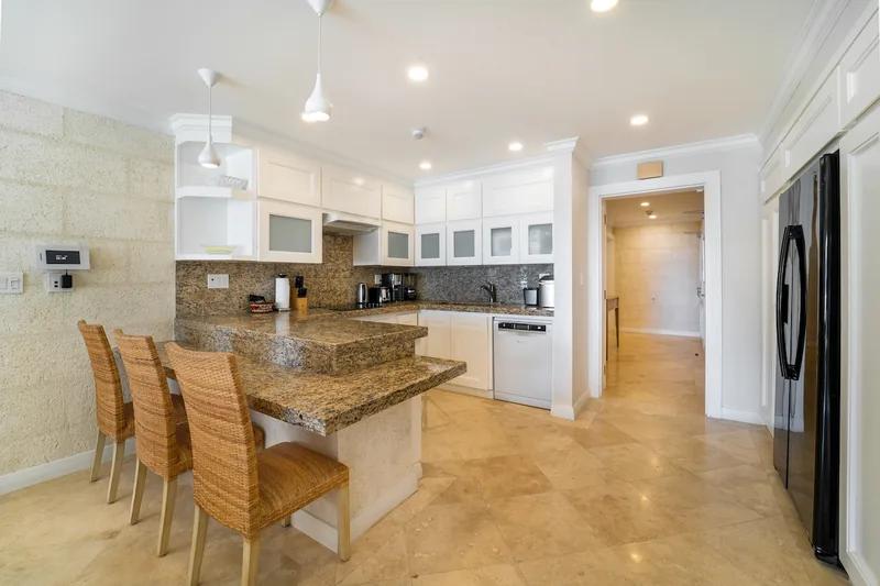 A kitchen with a granite breakfast bar and rattan stools under a white ceiling
