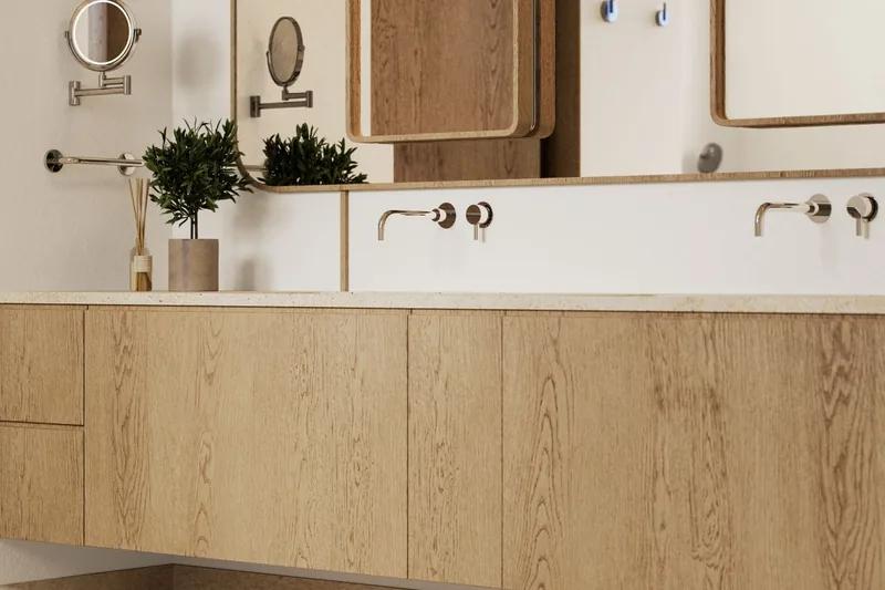 A pale timber vanity with round mirrors, wall taps and an olive branch in a vase