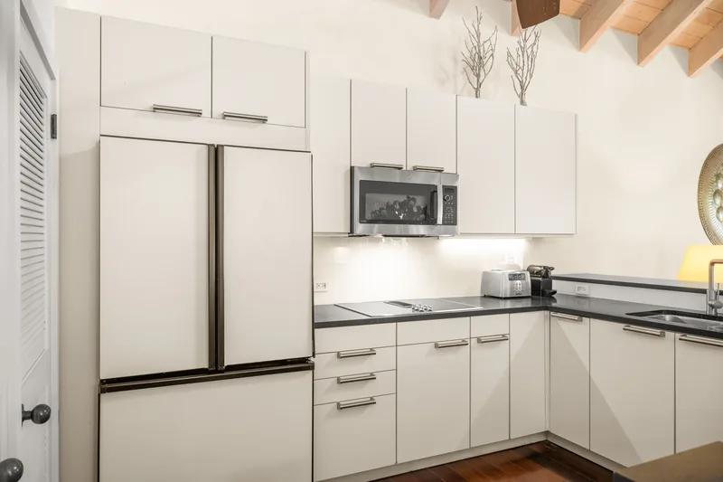 A white kitchen with full-height cabinets, a large fridge and dark stone worktops