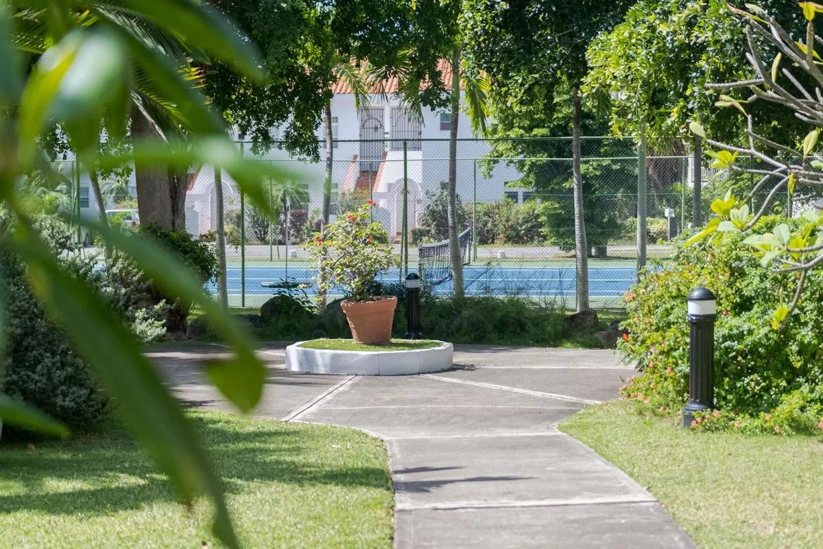 A curving garden path to a low stone fountain, a tennis court beyond the planting
