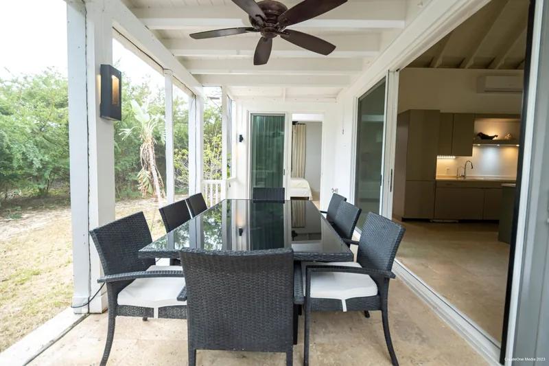 A covered terrace with a glass dining table, dark chairs and a ceiling fan