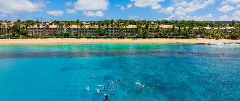 Swimmers in a turquoise Barbados bay, a low resort along the shore behind