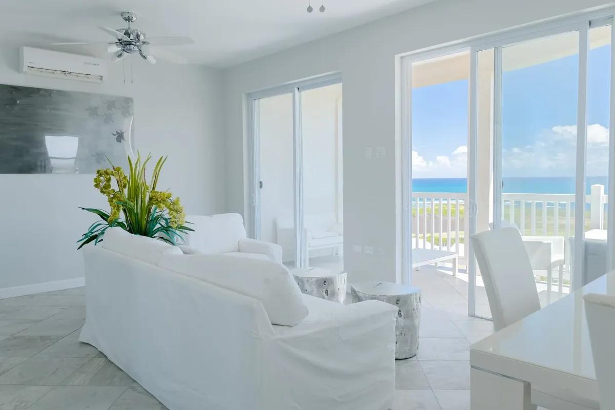 A white-furnished living room opening through sliding doors to a balcony above the Atlantic at Frigate Bay