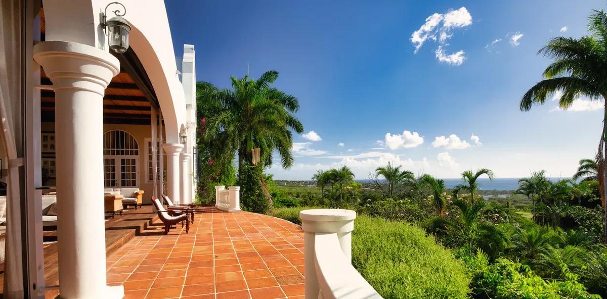 A terracotta-tiled colonnaded verandah looking out over palms and open country
