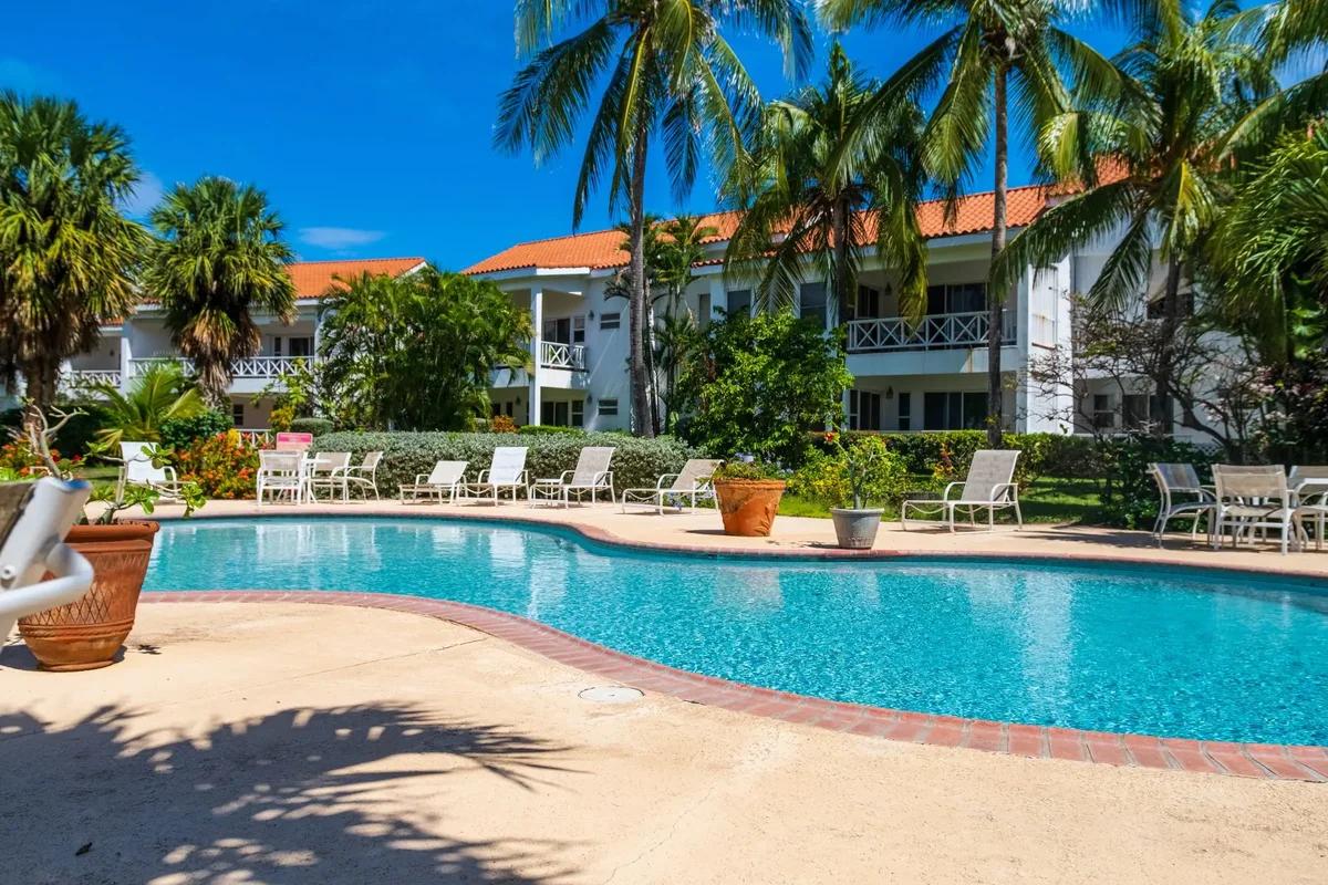 A resort pool ringed with loungers and palms, orange-roofed apartment buildings behind
